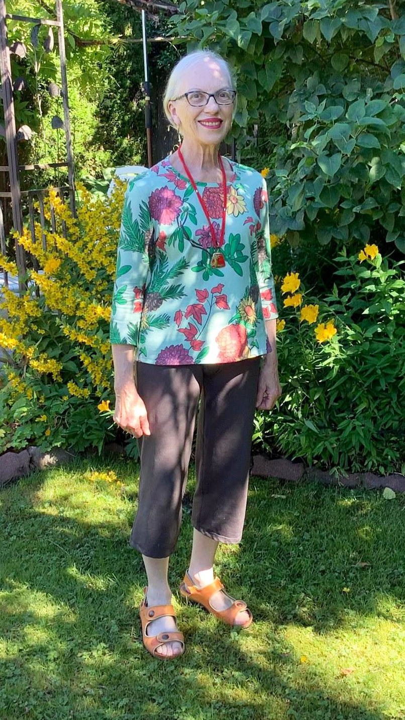 a woman standing in her garden, wearing a long sleeved top with a floral design