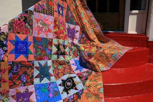 A hand made Kaffe Fasset pattern wedding quilt in fall colors draped over a red staircase
