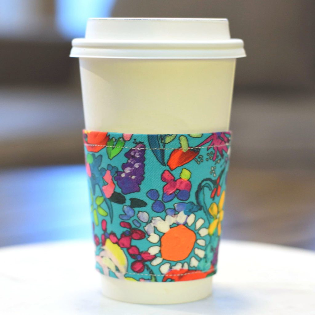 A white coffee cup with a colorful floral coffee sleeve