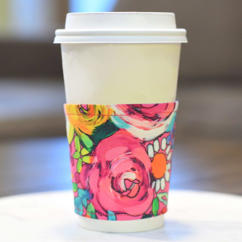 A white coffee cup with a colorful floral coffee sleeve 
