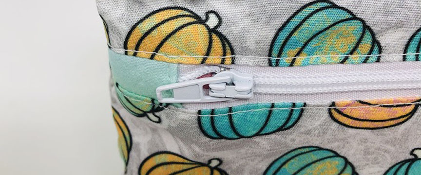 A white zipper sewn into some fabric with a pumpkin design